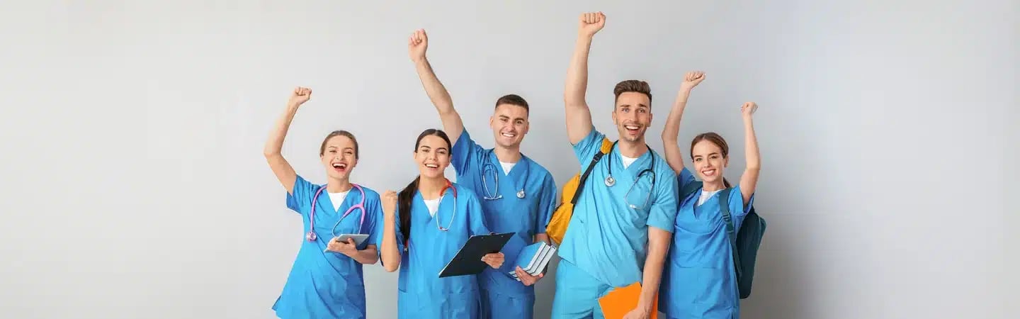 Five smiling medical professionals in scrubs, holding clipboards and notebooks, celebrate with raised fists.
