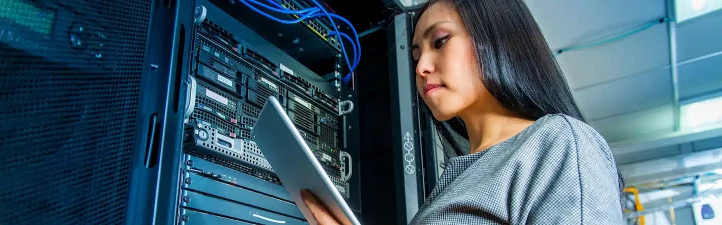 A woman holding a tablet works on a server rack in a data center.