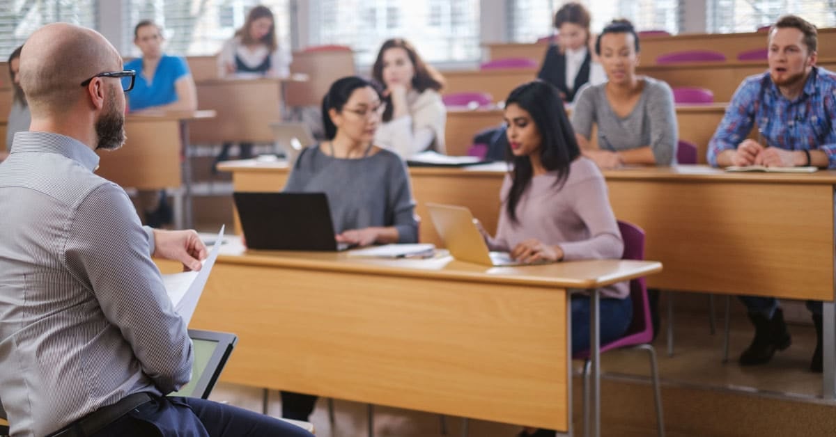 Instructor Spotlight: Gerard Lunow sits at the front of the classroom, engaging students as they listen attentively and take notes on their laptops and notebooks during his lecture.