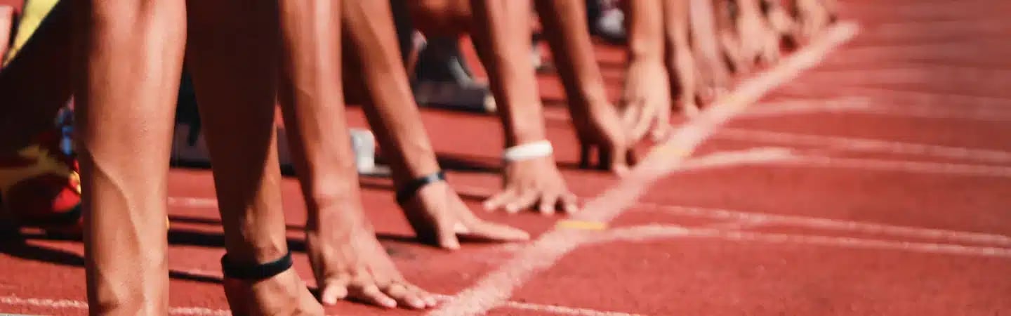 Athletes at the starting line on a track, poised with hands on the ground, ready to begin a race.