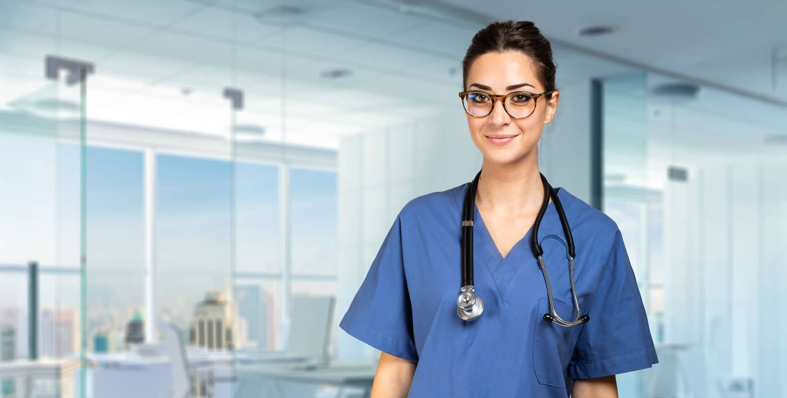 A smiling nurse in scrubs stands confidently in a modern medical office, symbolizing the comparison between night and day shifts in nursing.