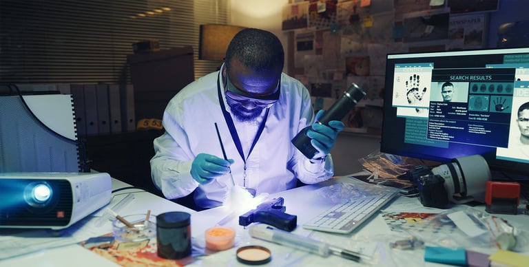 A forensic scientist in a lab coat examines evidence under UV light at a cluttered desk, surrounded by computers, documents, and forensic tools, searching for fingerprints.