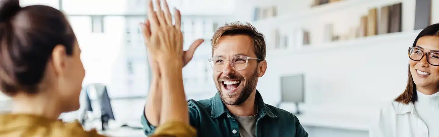 Three people smiling and celebrating with a high-five in a brightly lit office space.