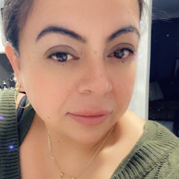 A selfie of a woman wearing gold hoop earrings and a thin gold necklace with an olive green sweater.