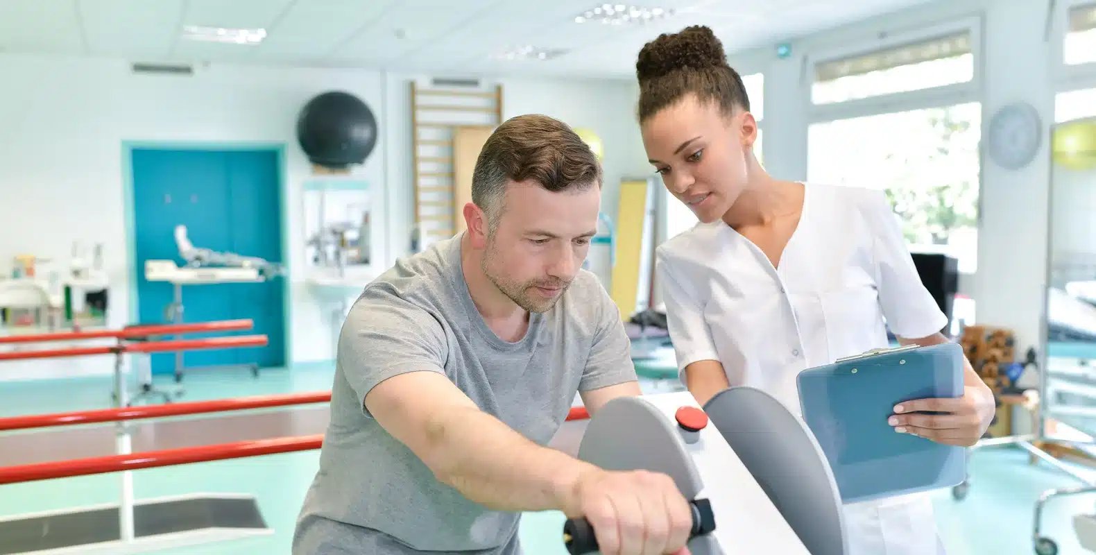 A physical therapist assists a man using exercise equipment in a rehabilitation center.