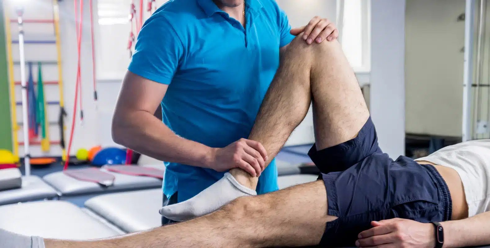 A physical therapist in a blue shirt helps a patient stretch their leg in a rehabilitation center.