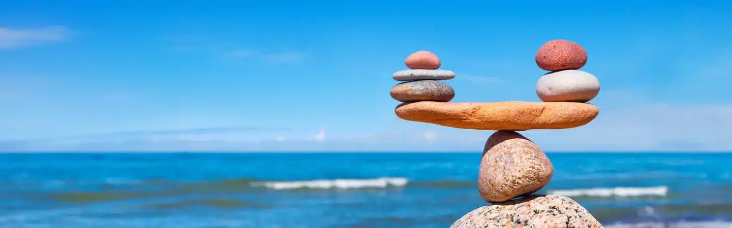 Stacked balanced stones on a beach with blue ocean waves and clear sky in the background.