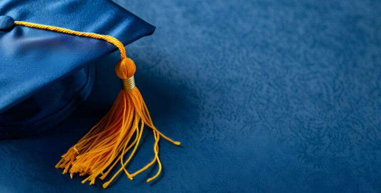 A blue graduation cap with a yellow tassel lies on a matching blue surface.