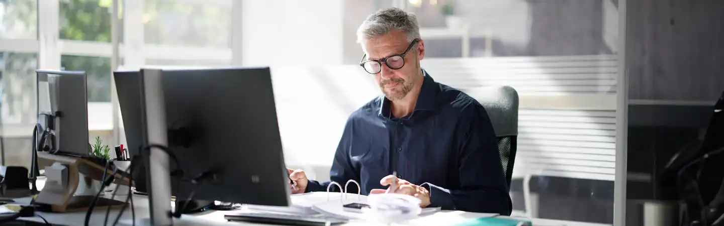 accountant wearing a blue shirt and black rimmed glasses working on his computer