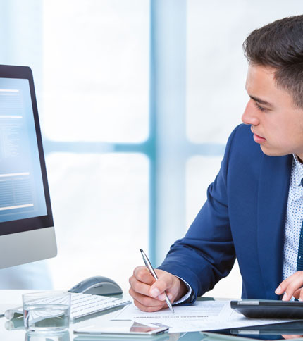 A focused man working at his computer while writing notes.