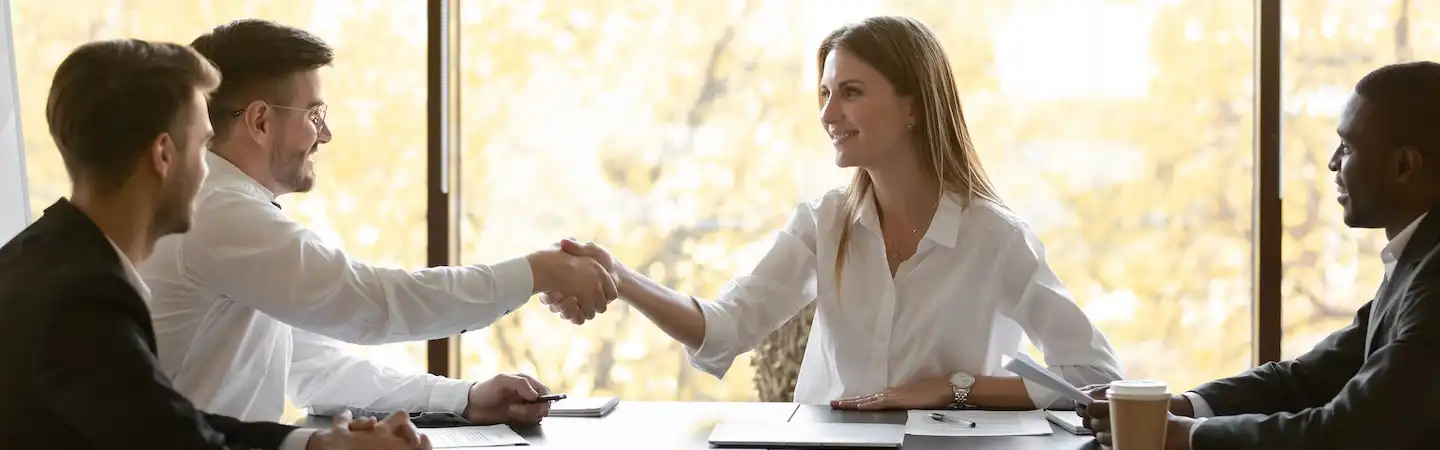 A person shaking hands with a person at a conference table.