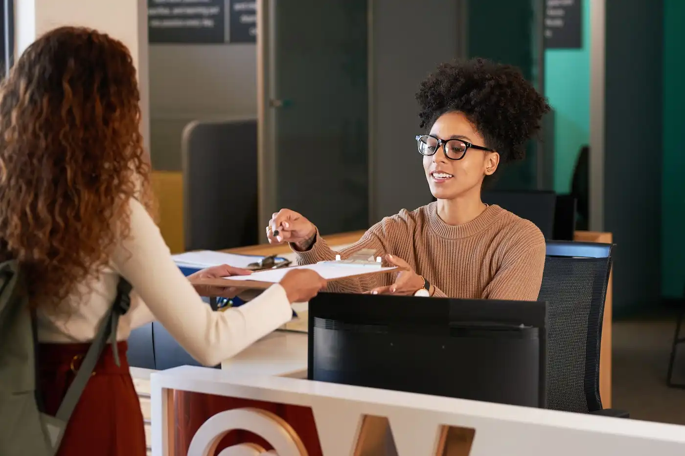 A receptionist handing a clipboard to a person in an office setting.