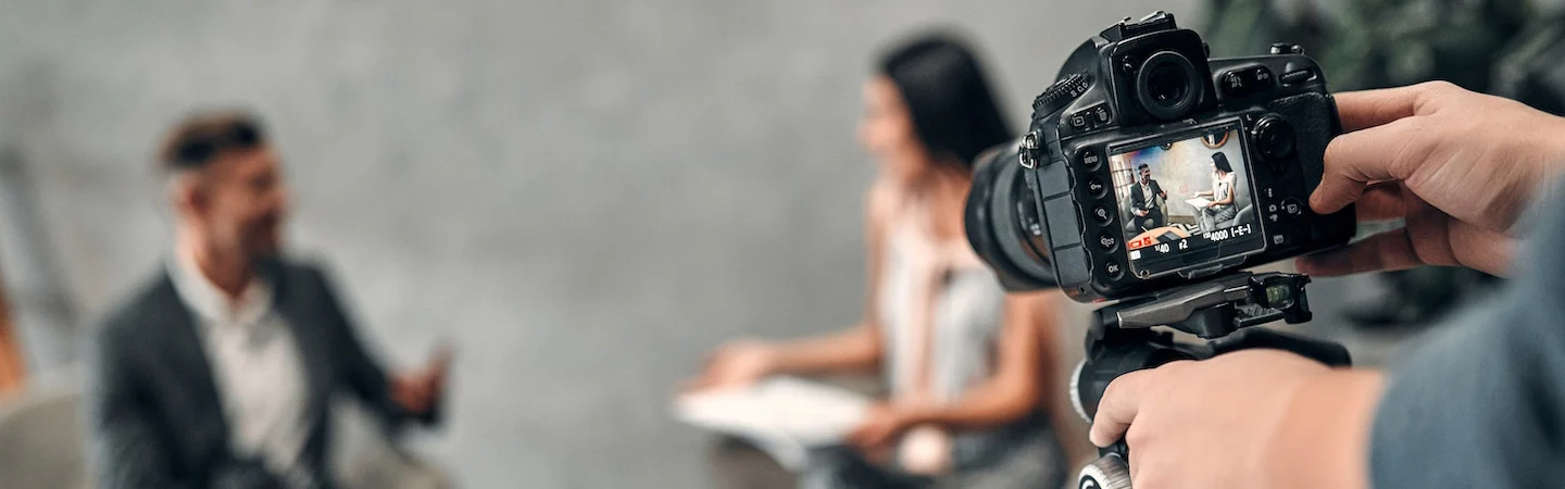 A camera focuses on two people sitting and talking, with one gesturing while the other looks at a paper.