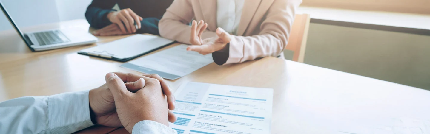 Business meeting with documents and a laptop on a table, featuring people in professional attire discussing.