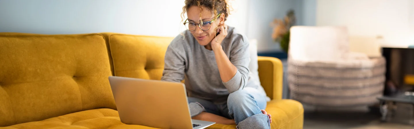 Person sitting on a yellow couch, using a laptop, with a cozy interior background.