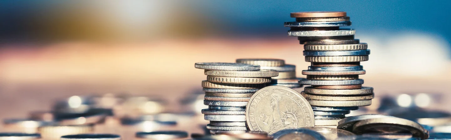 Stacks of various coins on a blurred background with scattered coins around.