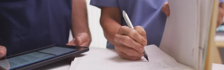 Close-up of medical professionals writing on a clipboard and using a tablet.