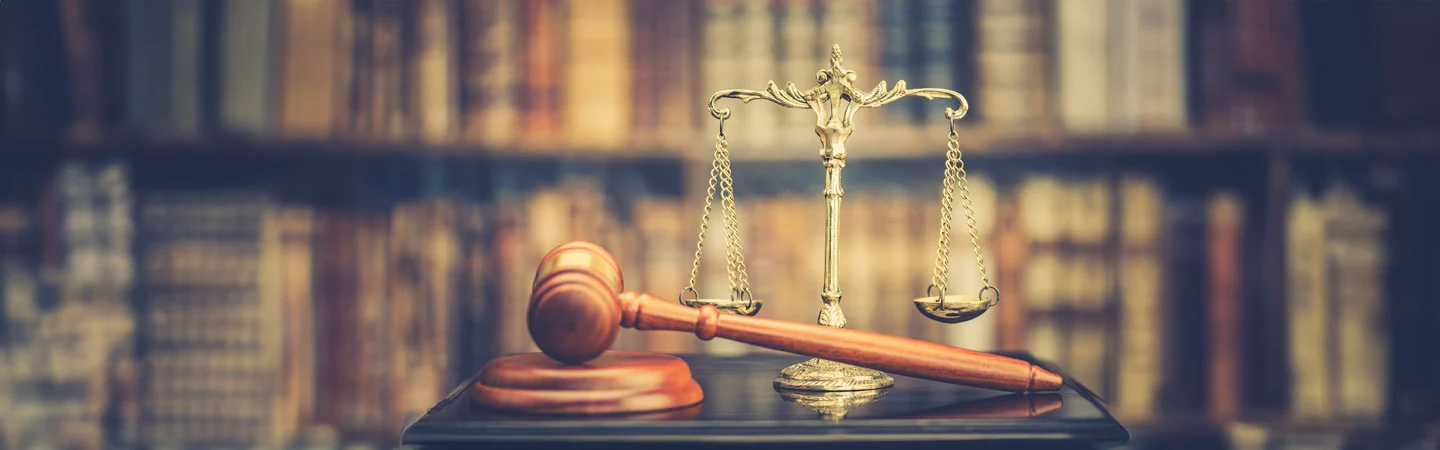 A gavel and a brass scale of justice in front of a blurred background of books on a shelf.