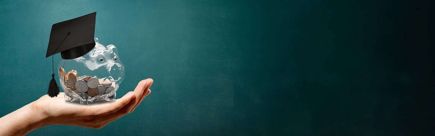 Hand holding a piggy bank with coins and a graduation cap on a teal background, symbolizing education savings.