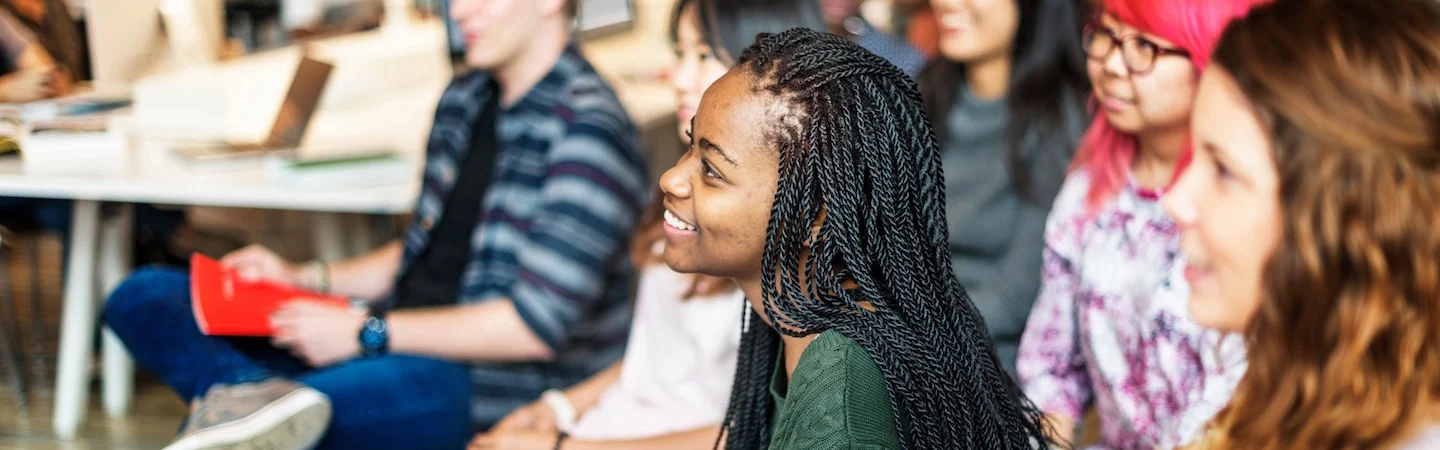 A group of diverse people sitting and smiling in a classroom setting.