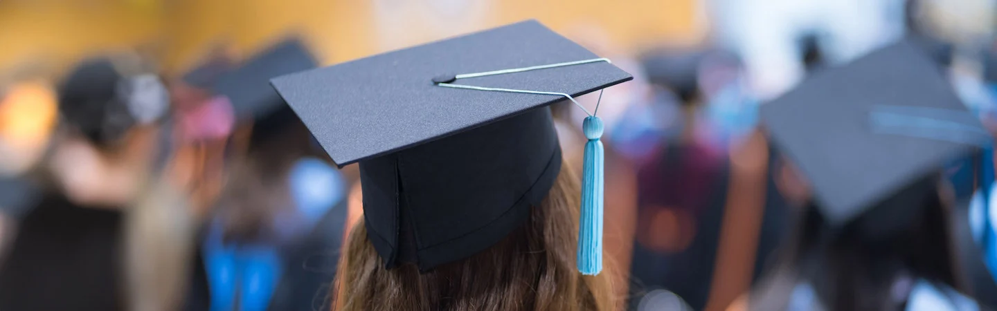 Close-up of a graduate's cap with a blue tassel during a graduation ceremony, with other graduates in the background.