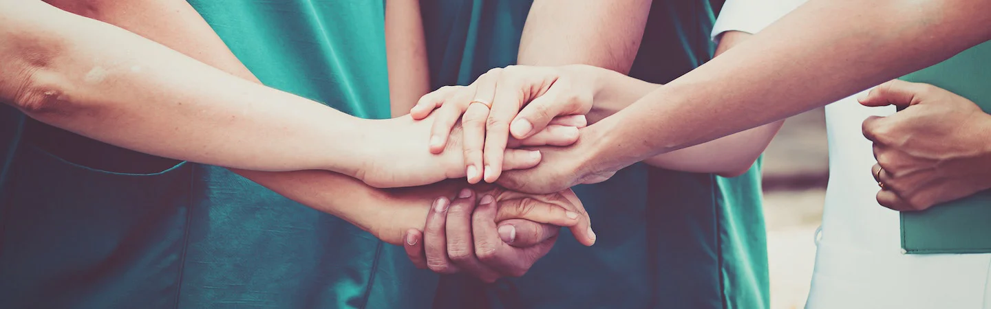 A group of people wearing green uniforms place their hands together in a unified show of teamwork and support.