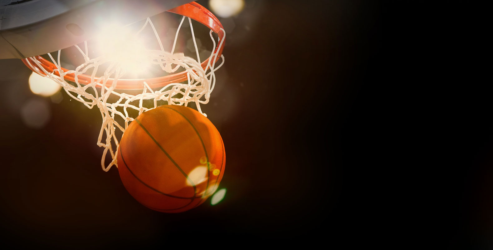 A basketball going through a hoop, captured mid-action with dramatic lighting in the background.