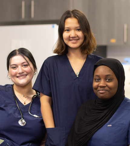 Three women in medical scrubs smiling.