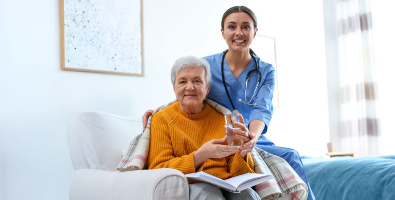 A smiling nurse in blue scrubs helps an elderly woman wrapped in a blanket, showcasing unique nursing roles in home healthcare settings