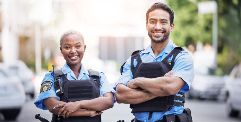 Two police officers standing together, smiling in their uniforms.