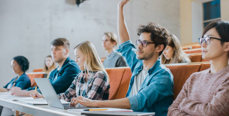 A college lecture hall with a student raising his hand to ask a question.