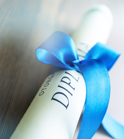 A rolled-up diploma tied with a blue ribbon lies on a wooden surface.